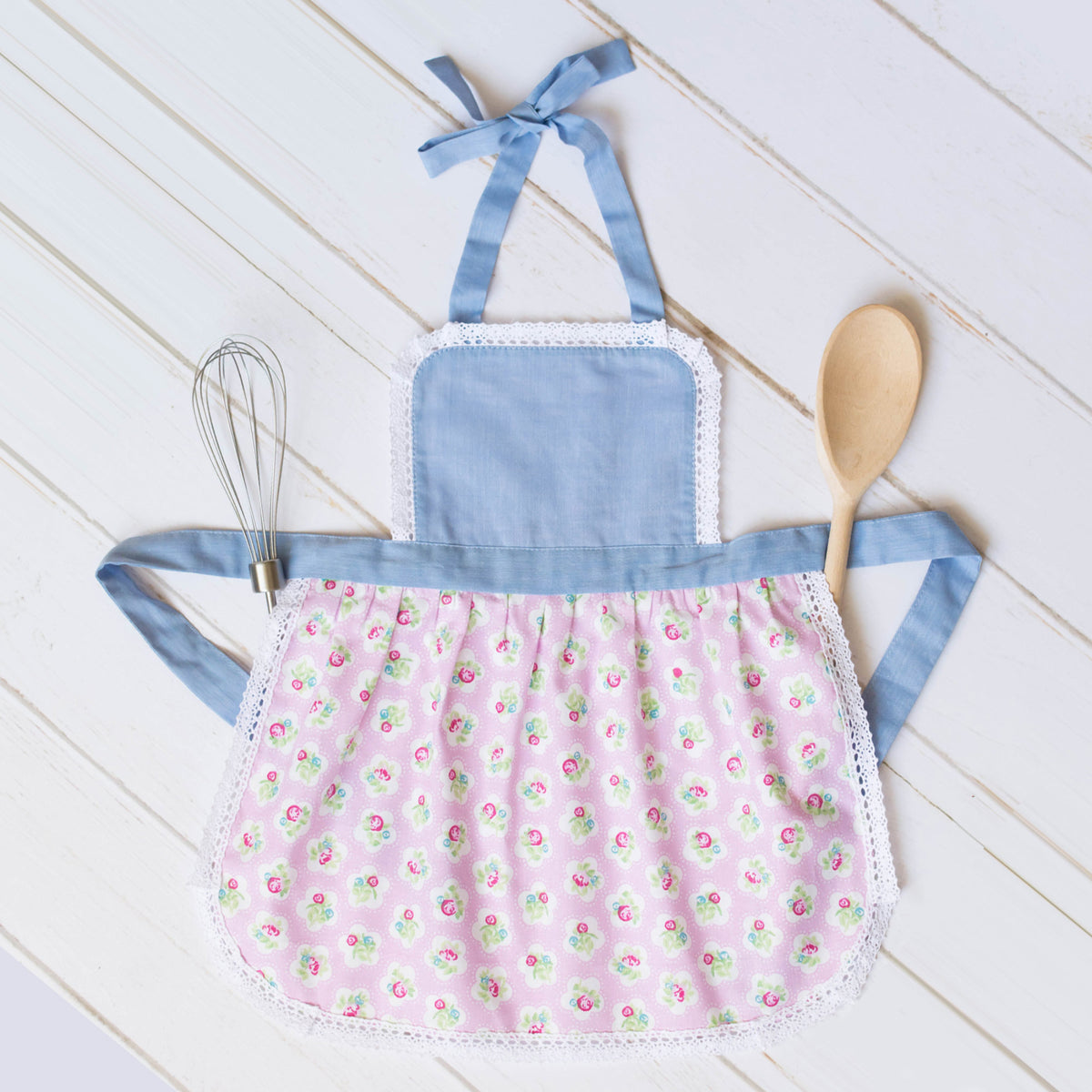 Baby and toddler apron with lace trim, flat lay with wooden spoon