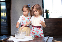 Two girls baking together in floral kids aprons